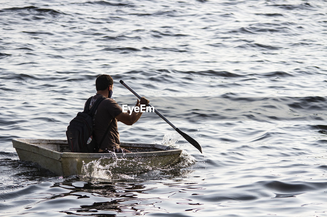 Rear view of man wearing mask sitting on boat in lake