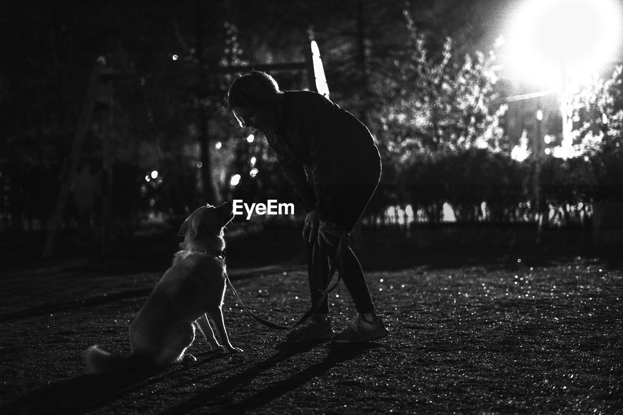 Young woman playing with dog in park at night