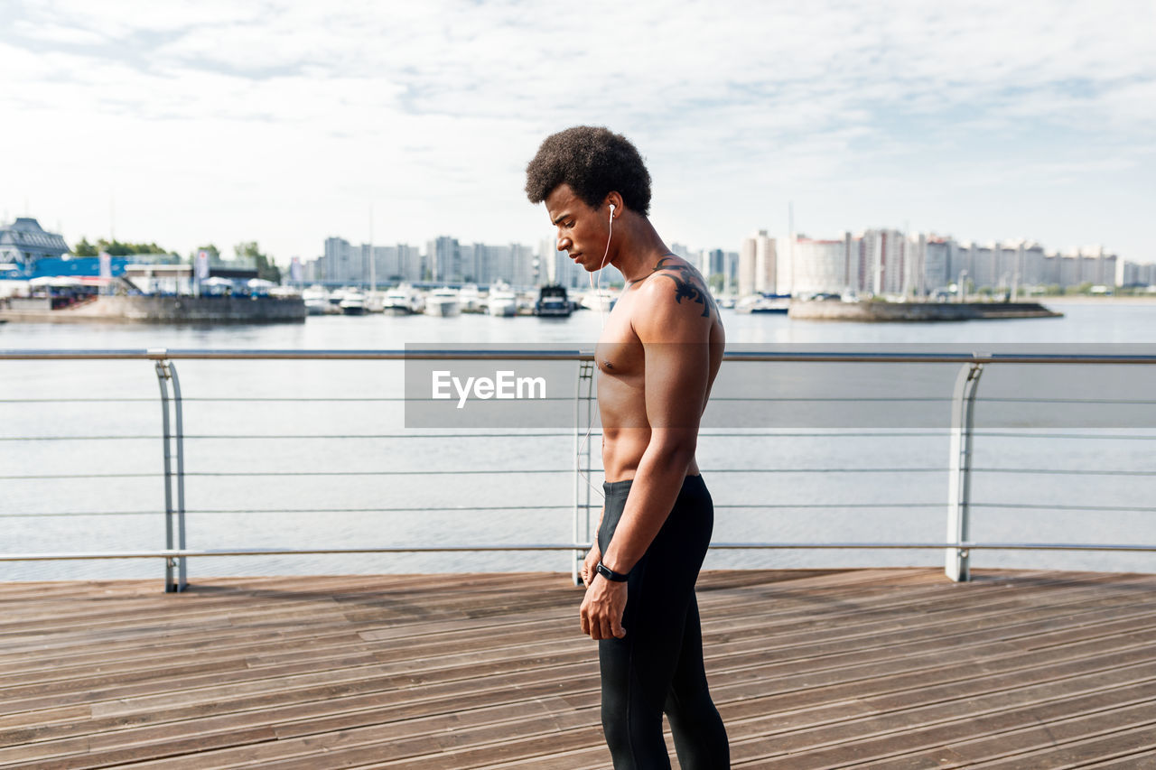 Side view of shirtless male athlete standing on promenade in city