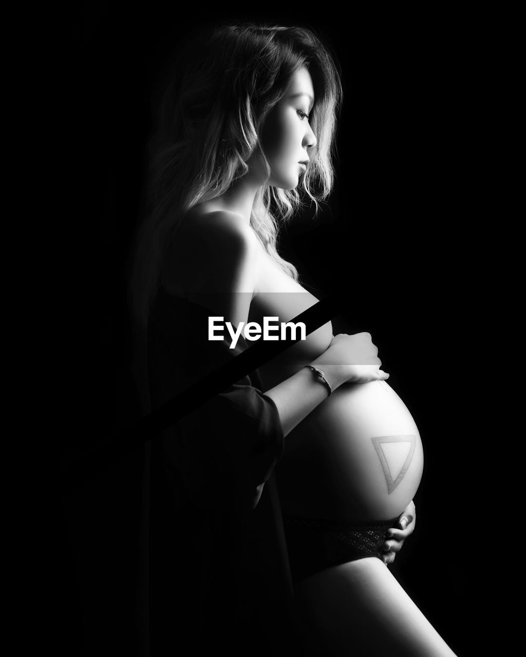 Side view of sensuous pregnant woman standing against black background