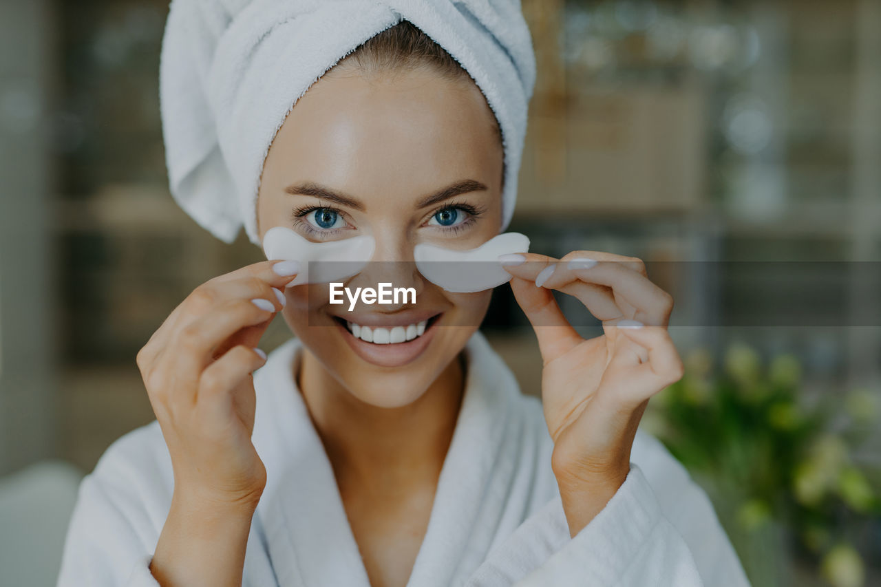 Portrait of young smiling woman holding medical eye patches at home