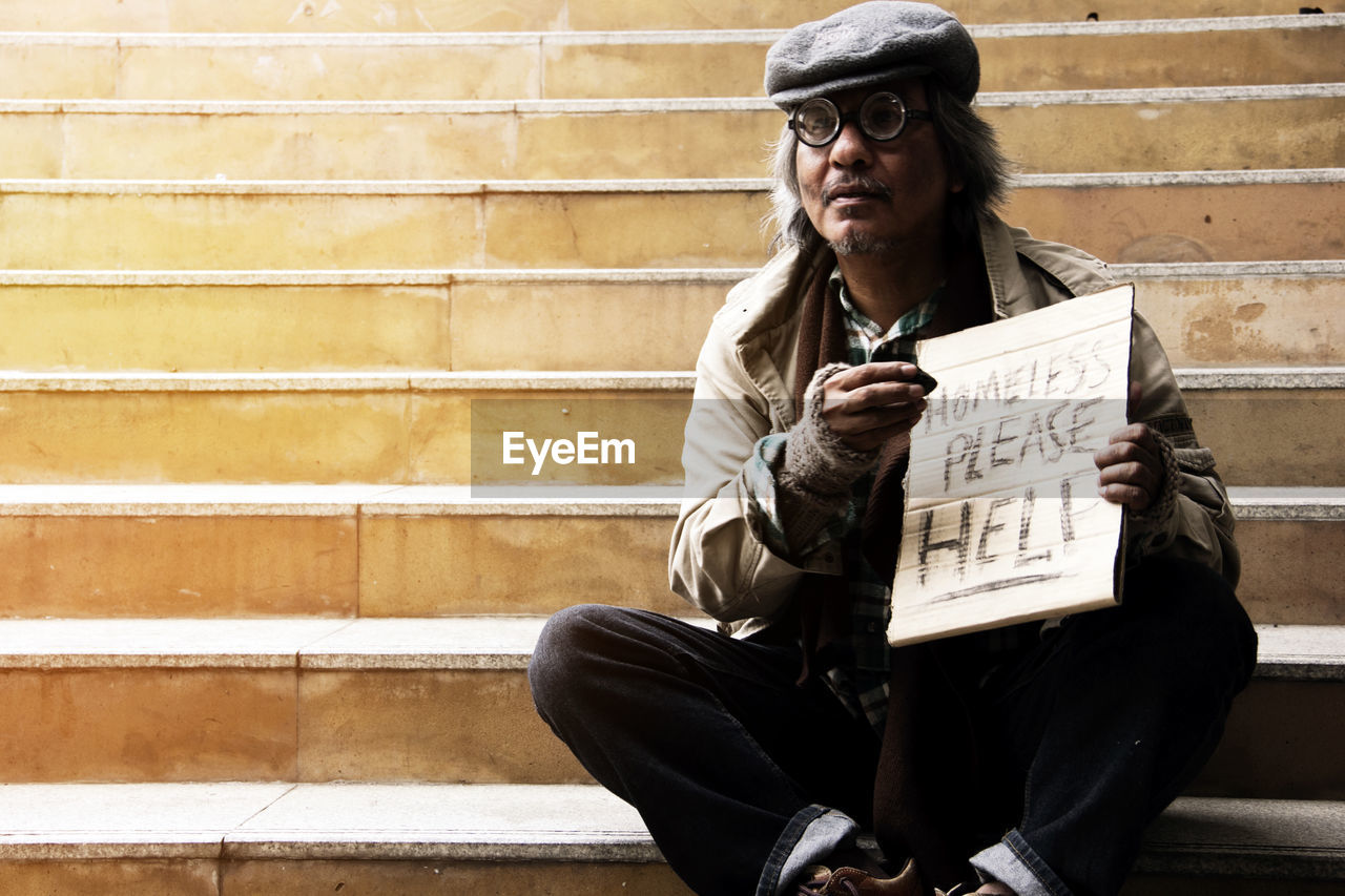 Beggar with text on cardboard sitting on steps