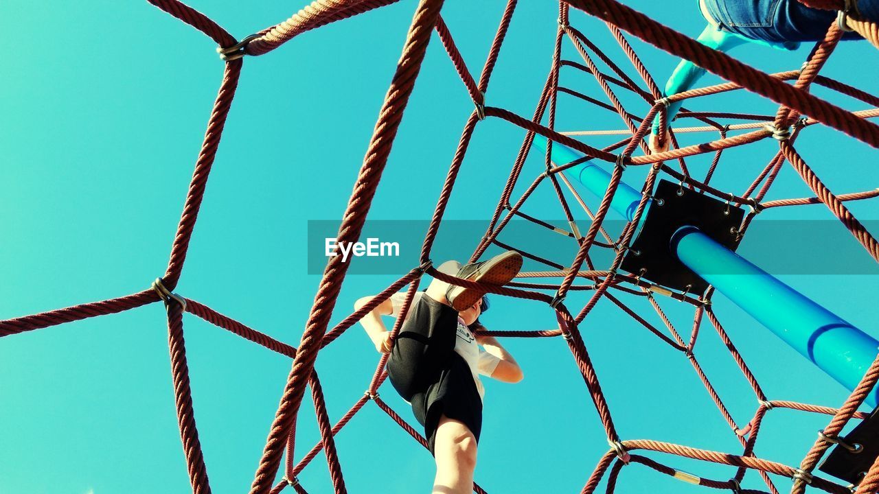 Low angle view of woman climbing on ropes at playground against clear sky