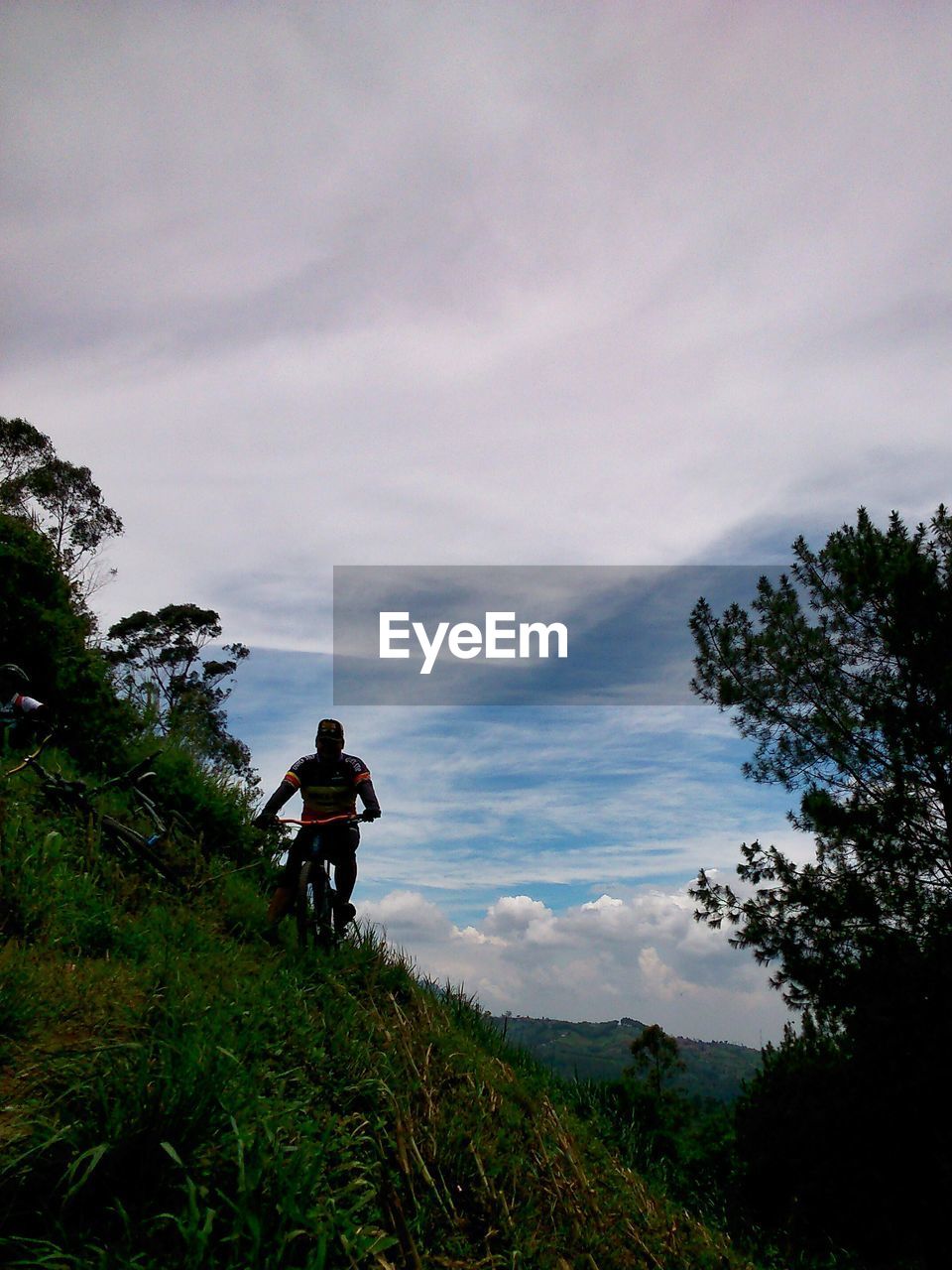 Man riding bicycle on mountain against cloudy sky