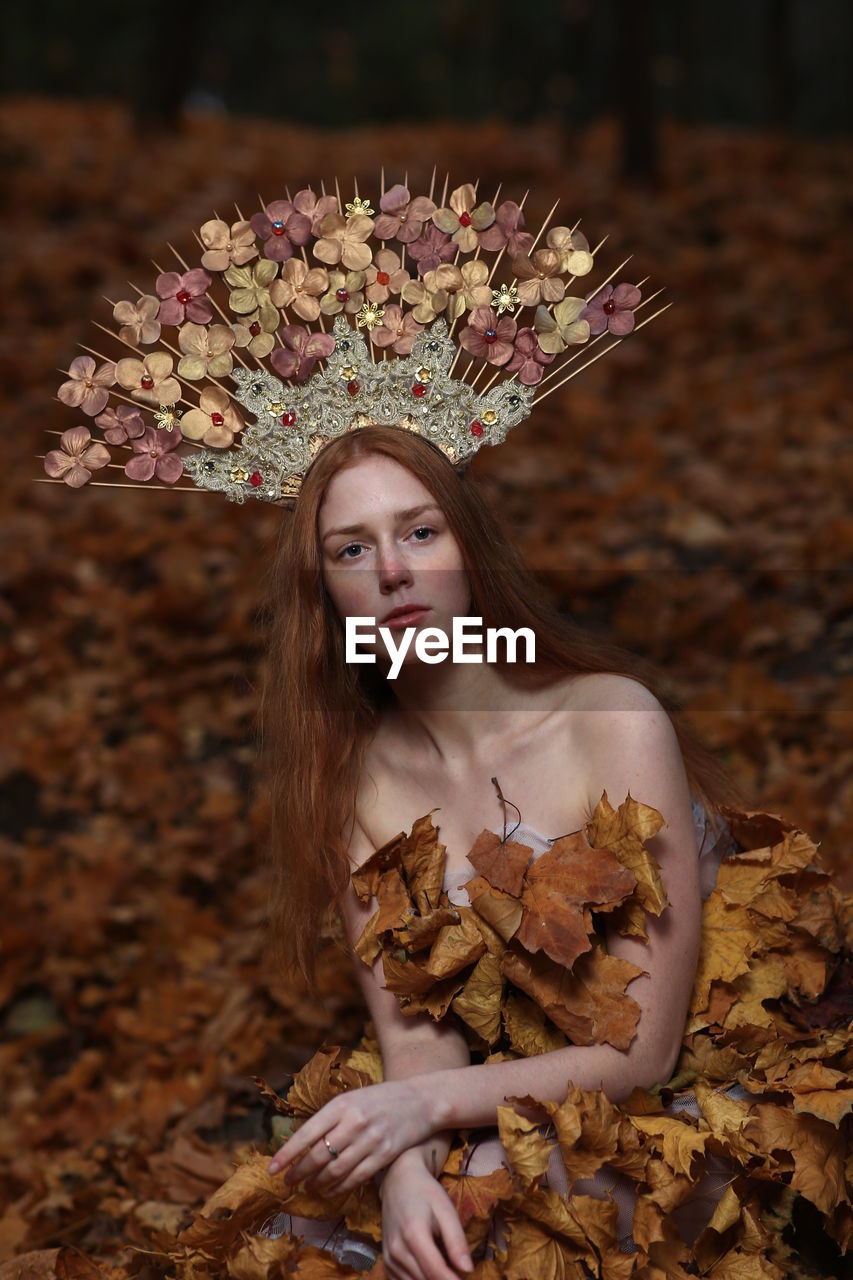 Portrait of young woman wearing flowers on hair sitting at forest during autumn