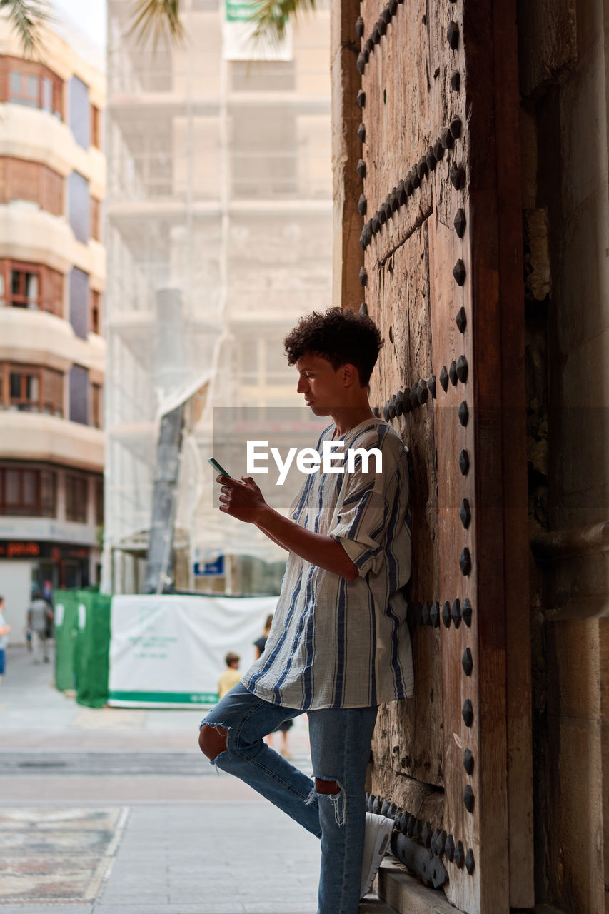 Young afro leaning on a wooden gate looking at his phone