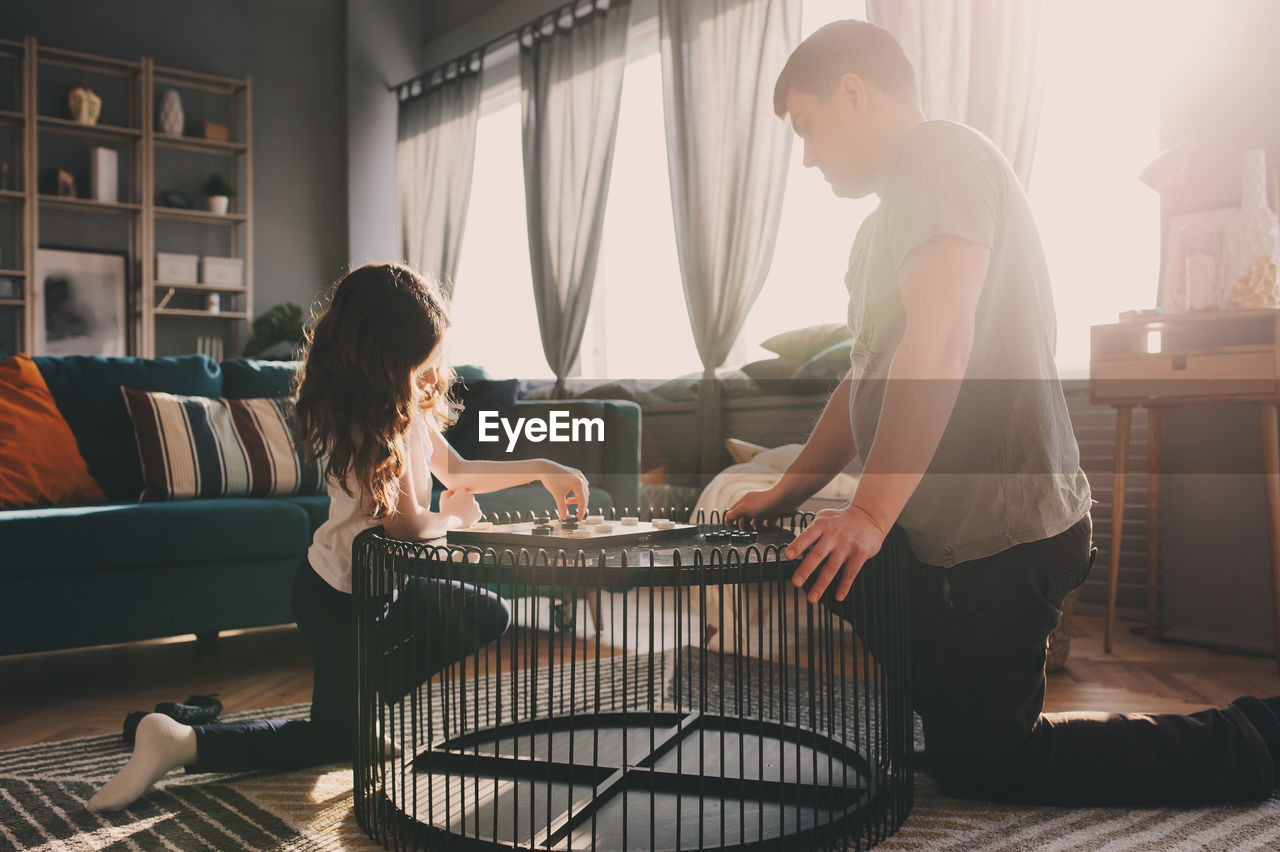 Girl playing checkers with father on table at home