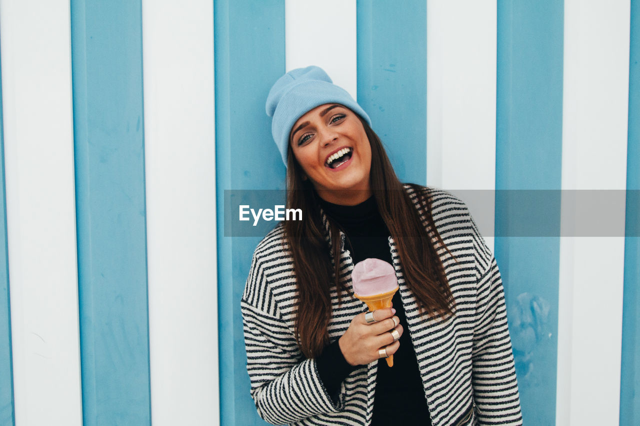 Portrait of cheerful woman having ice cream cone by striped wall