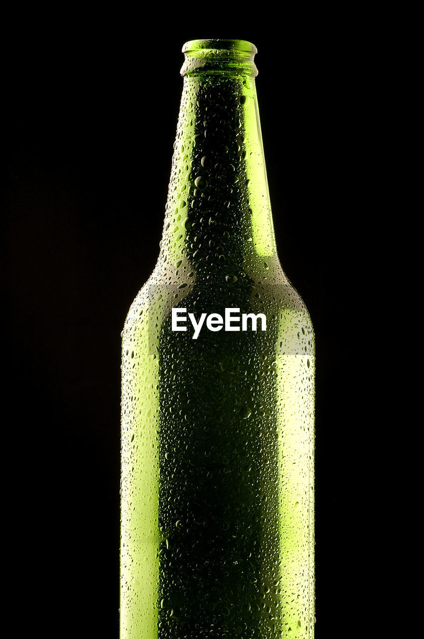 CLOSE-UP OF GLASS OF BOTTLE AGAINST BLACK BACKGROUND