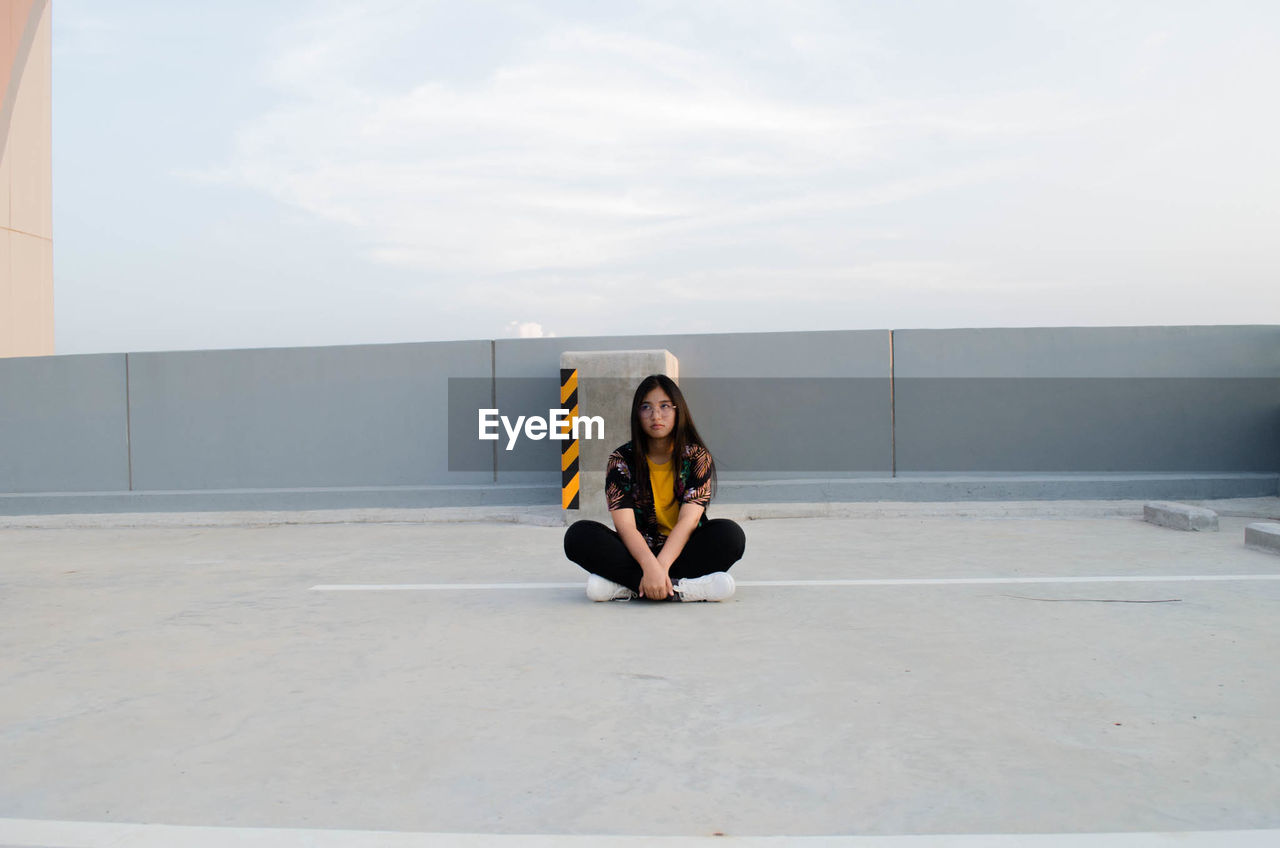 Portrait of young woman sitting on road against sky