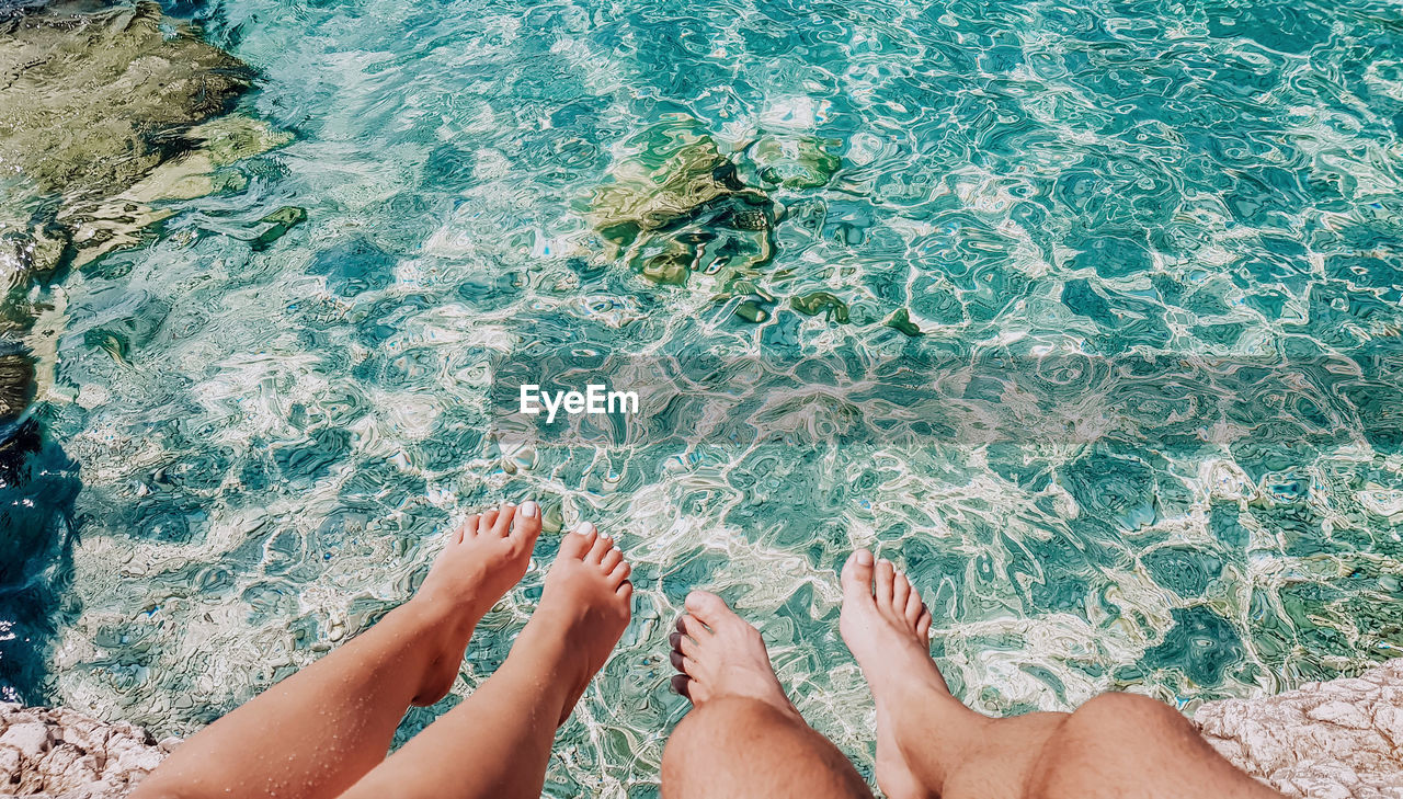 Personal perspective of young couple dangling feet above water on beach.