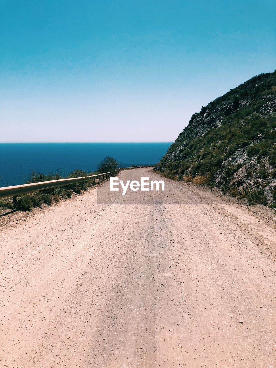 Road by sea against clear blue sky