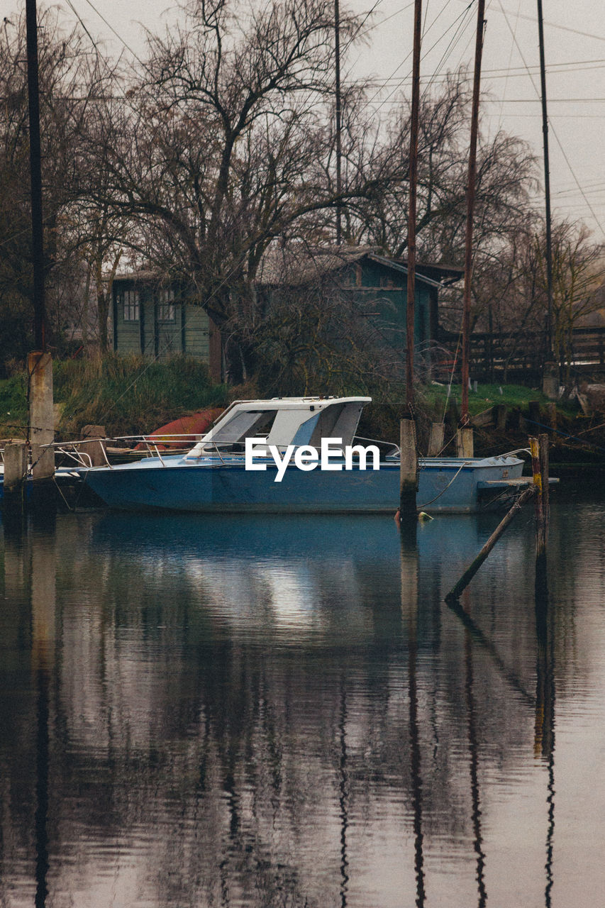 SAILBOATS MOORED IN LAKE AGAINST BARE TREES