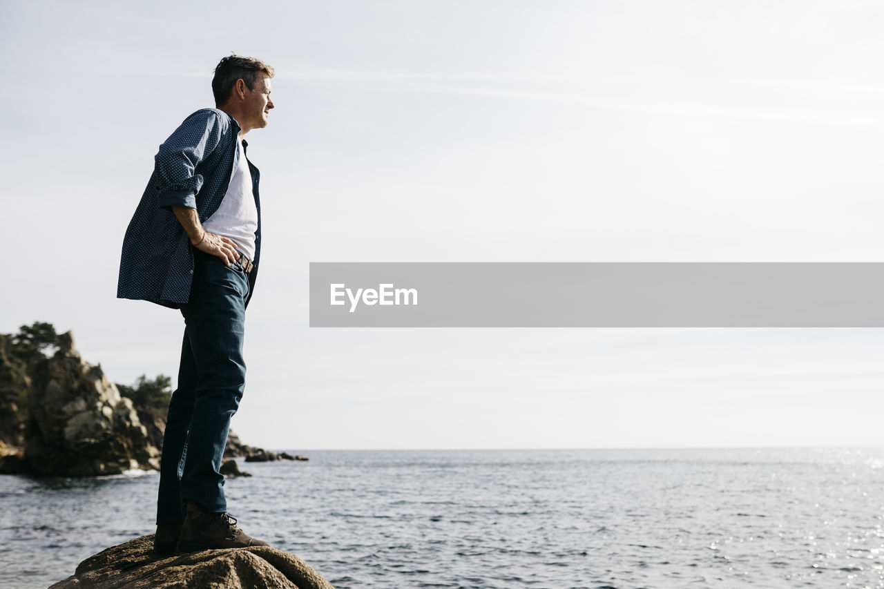 Man looking away while standing on rock against clear sky