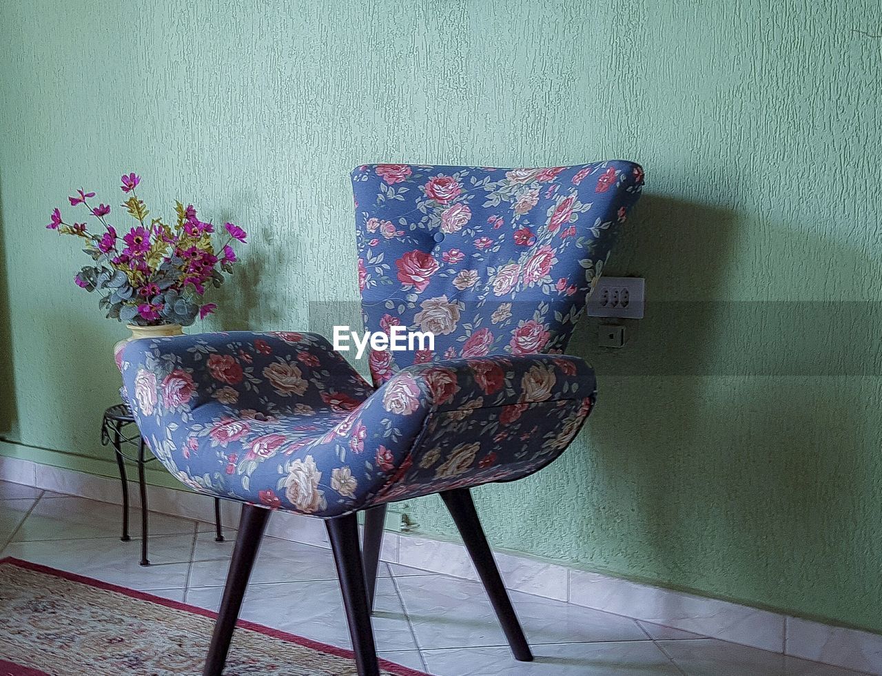 Empty floral pattern chair by green wall at home