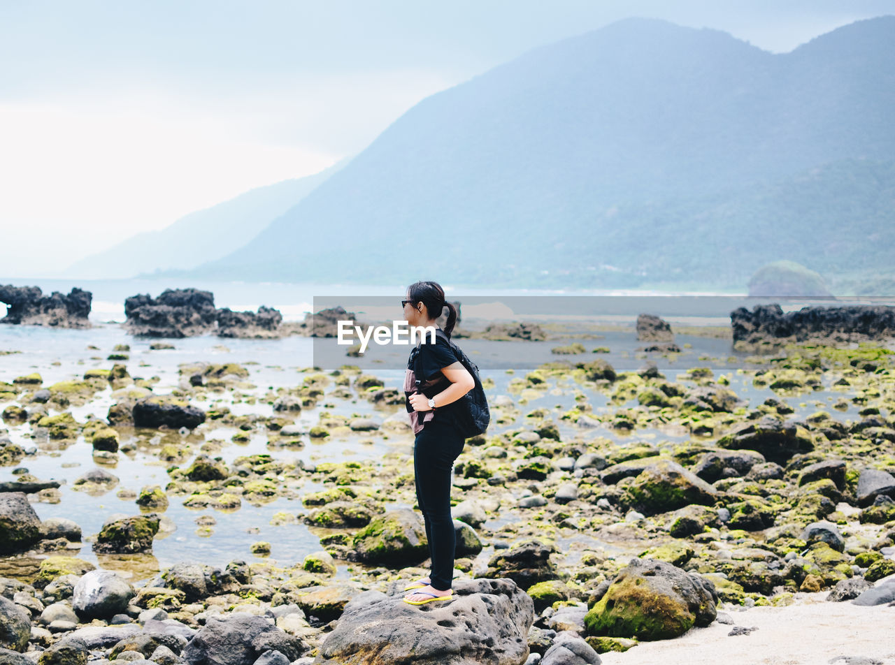 Rear view of woman standing on beach against sky