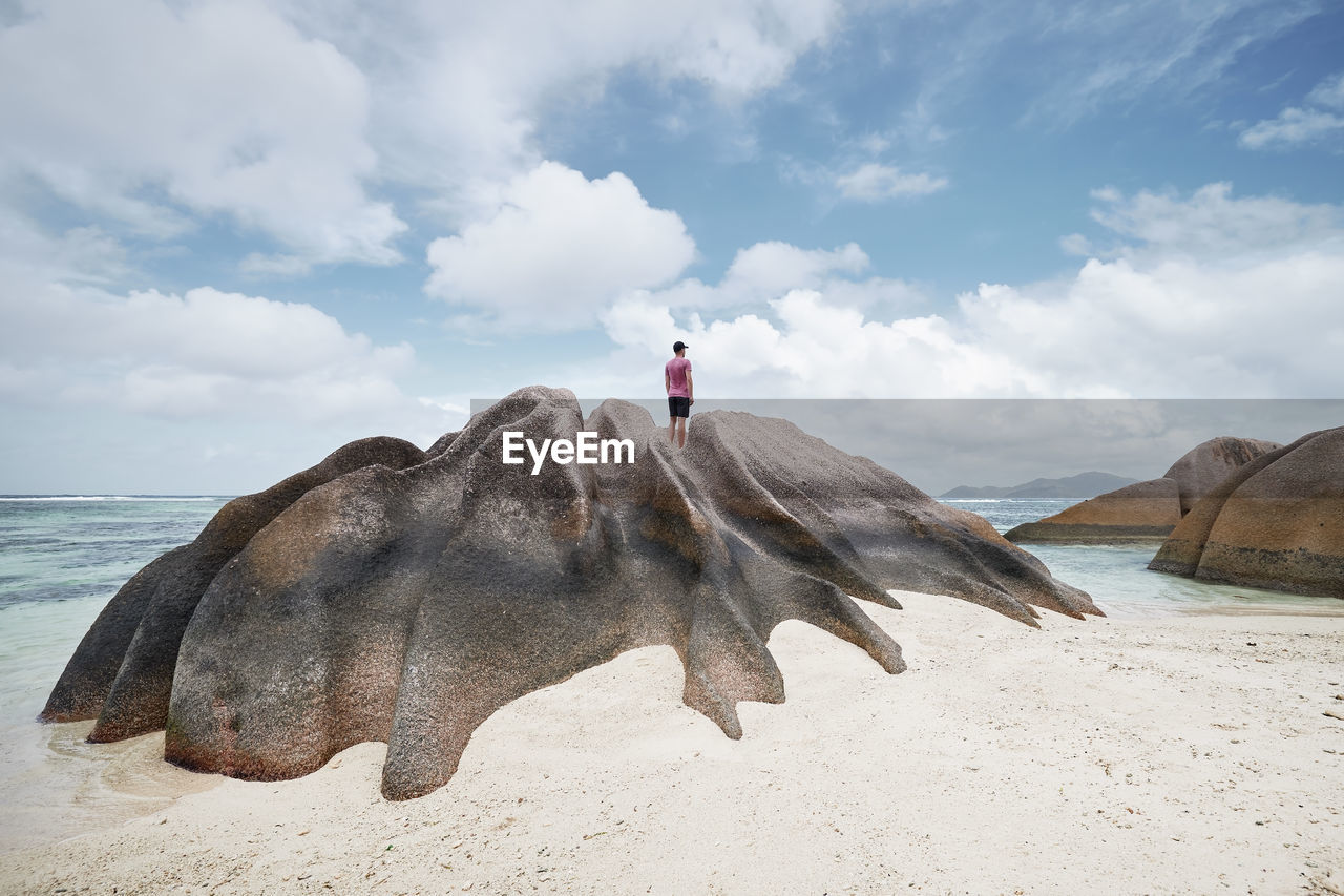 Man standing on rock and looking at view. lonely tourist enjoying calm on beach in seychelles.