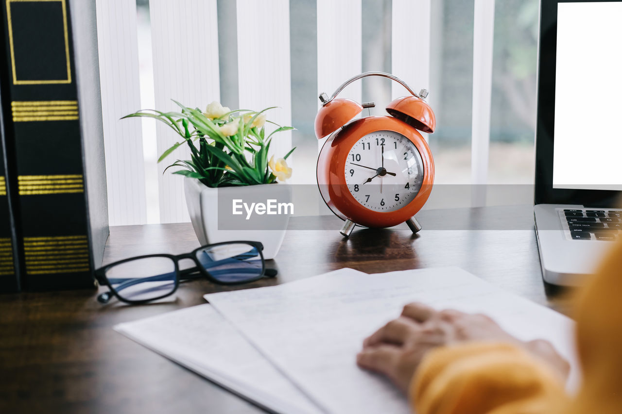 Man walking by laptop with alarm clock on table at home