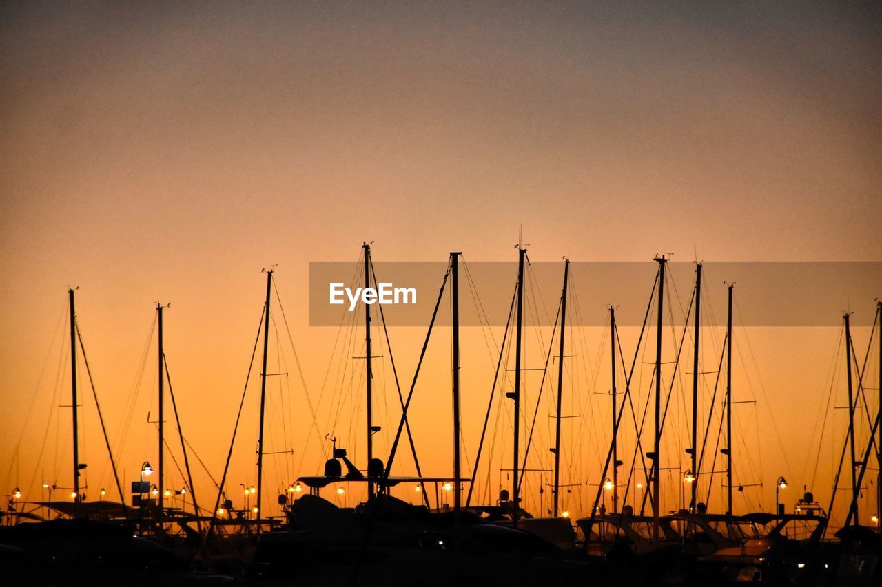 Silhouette sailboats in harbor against sky during sunset