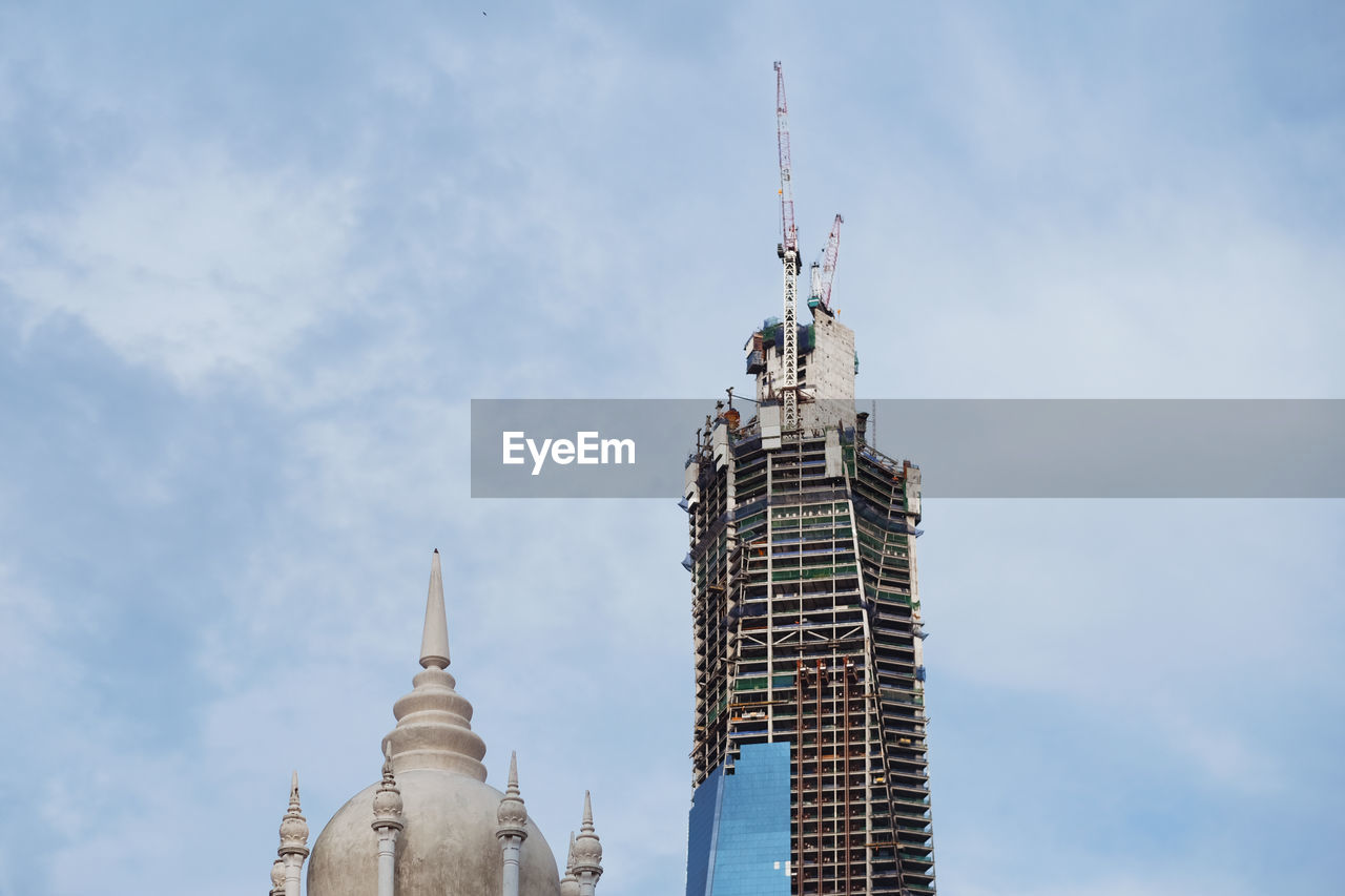 Low angle view of old and new building against cloudy sky