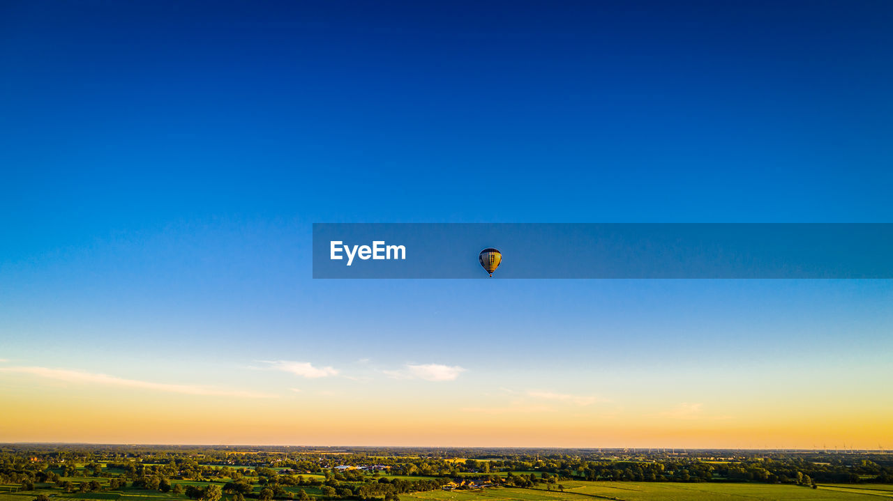 Hot air balloons flying over land against sky during sunset