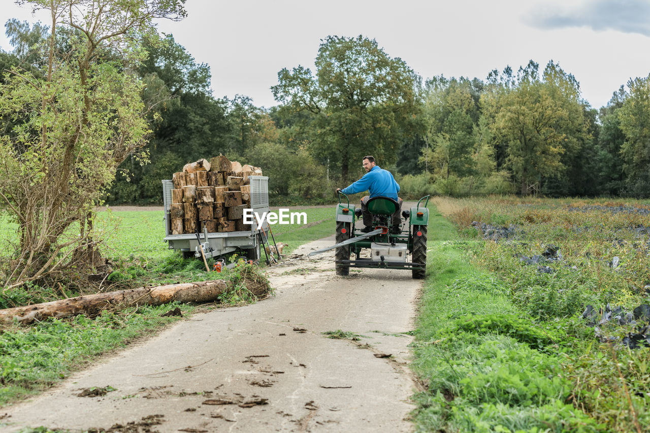 REAR VIEW OF MAN RIDING MOTORCYCLE ON ROAD AMIDST TREES