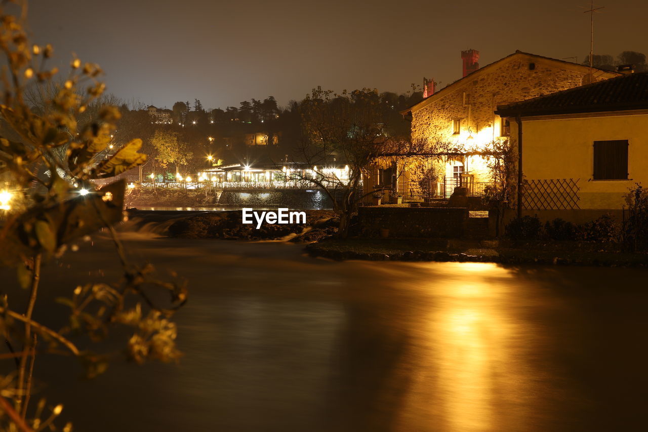 ILLUMINATED BUILDINGS BY RIVER AT NIGHT