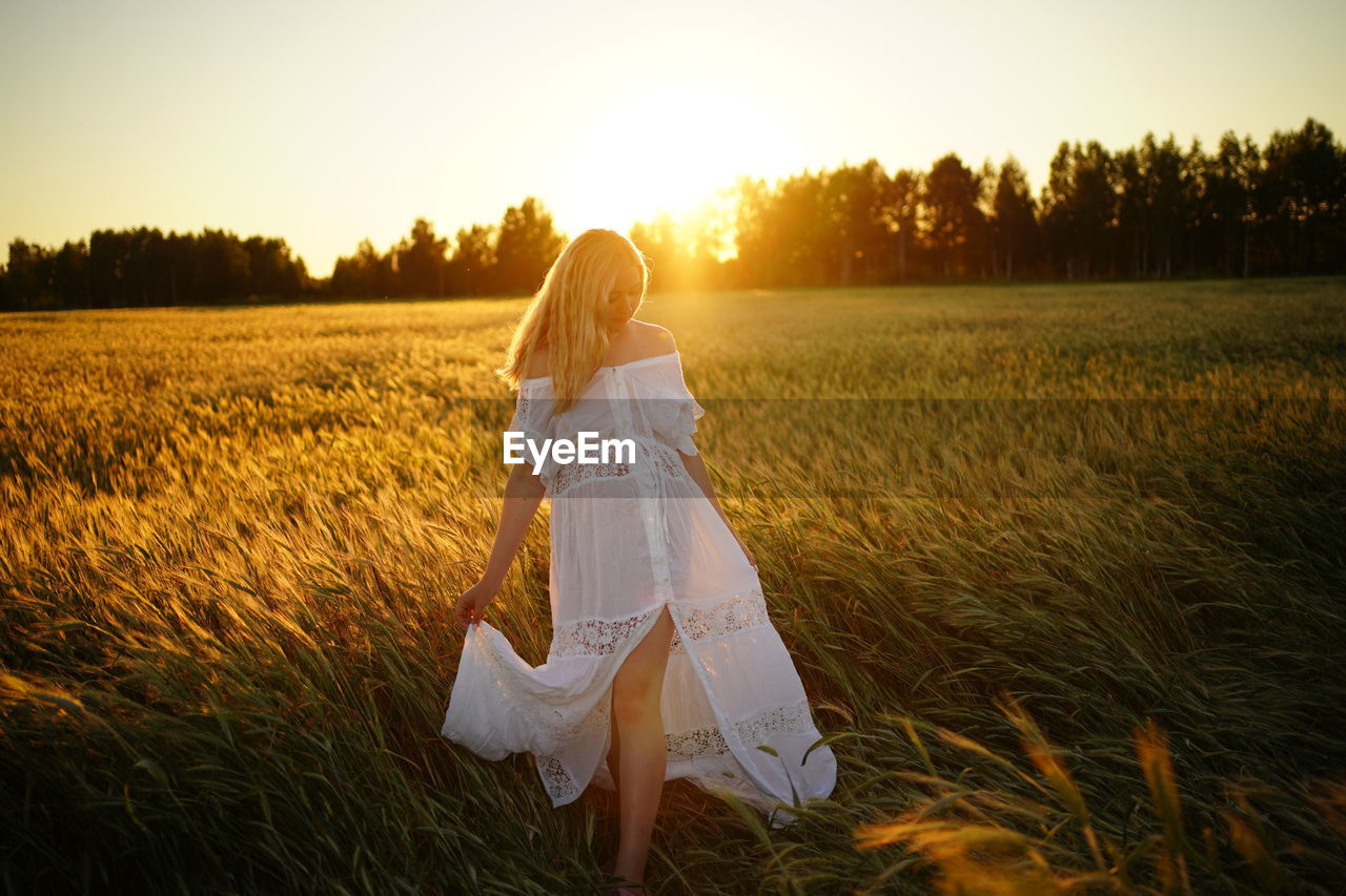 Rear view of woman walking on field against sky during sunset