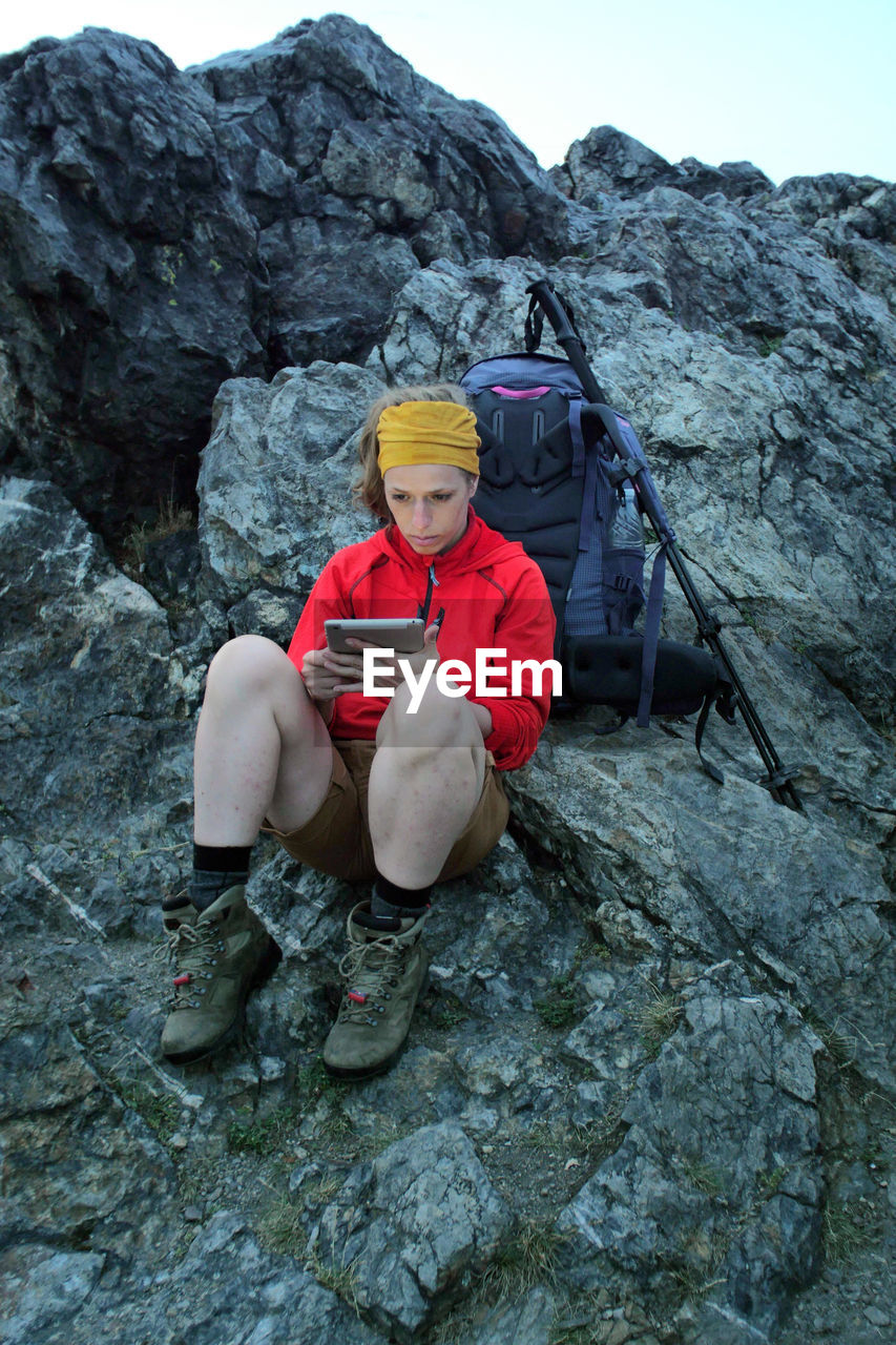 Full length of woman using digital tablet while sitting on rock formation