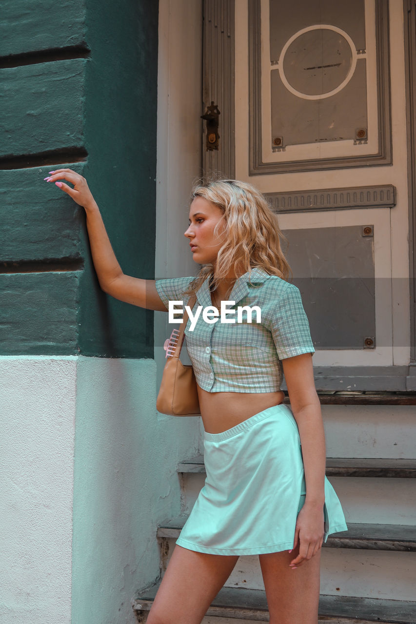 Woman looking away while standing against wall