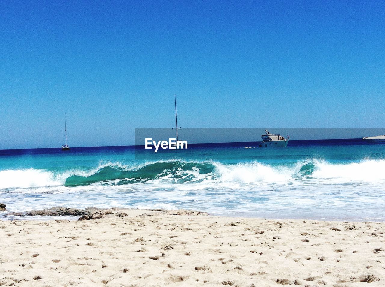 Sea waves splashing on beach against clear blue sky