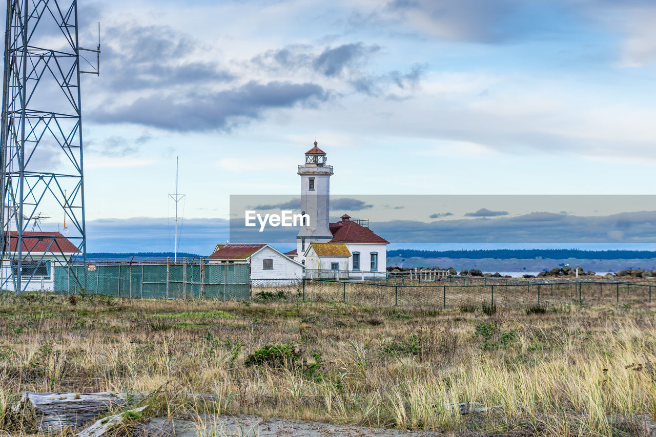 LIGHTHOUSE AMIDST BUILDINGS AGAINST SKY