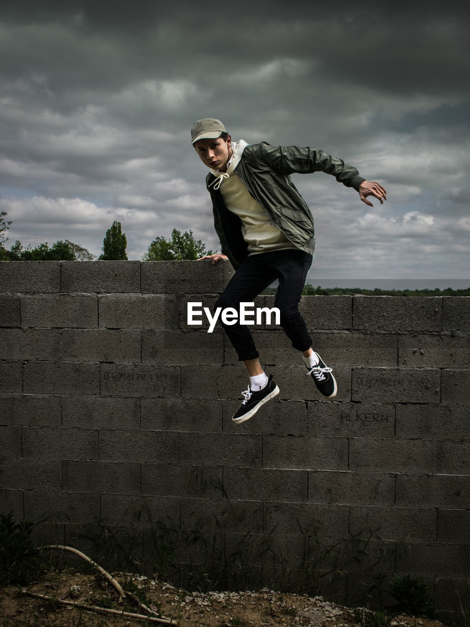 Full length of man jumping from wall against cloudy sky