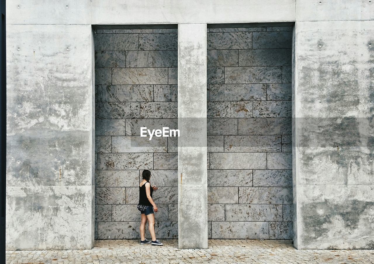 Full length of woman standing by concrete wall