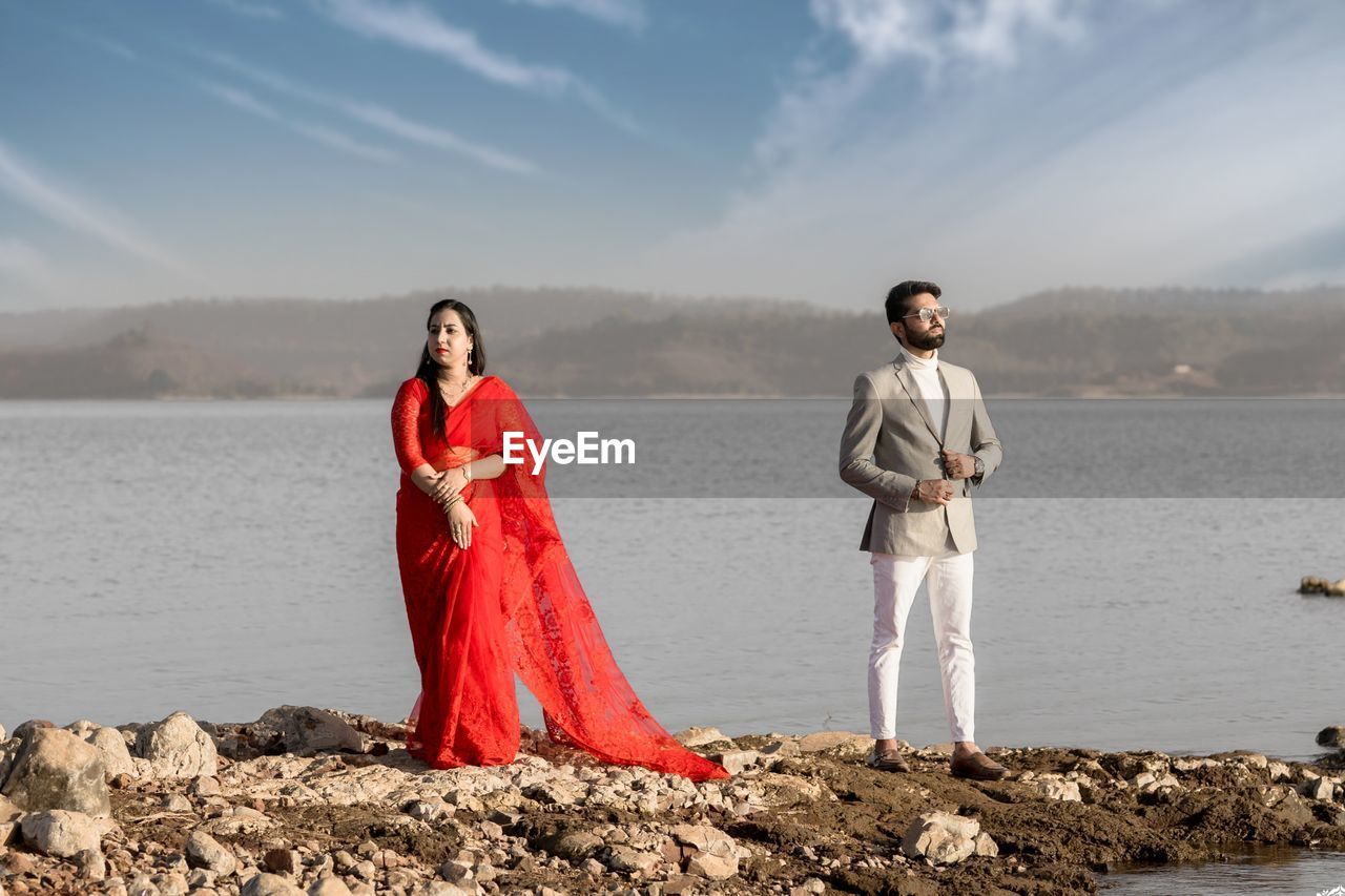 Young couple standing on shore against sky