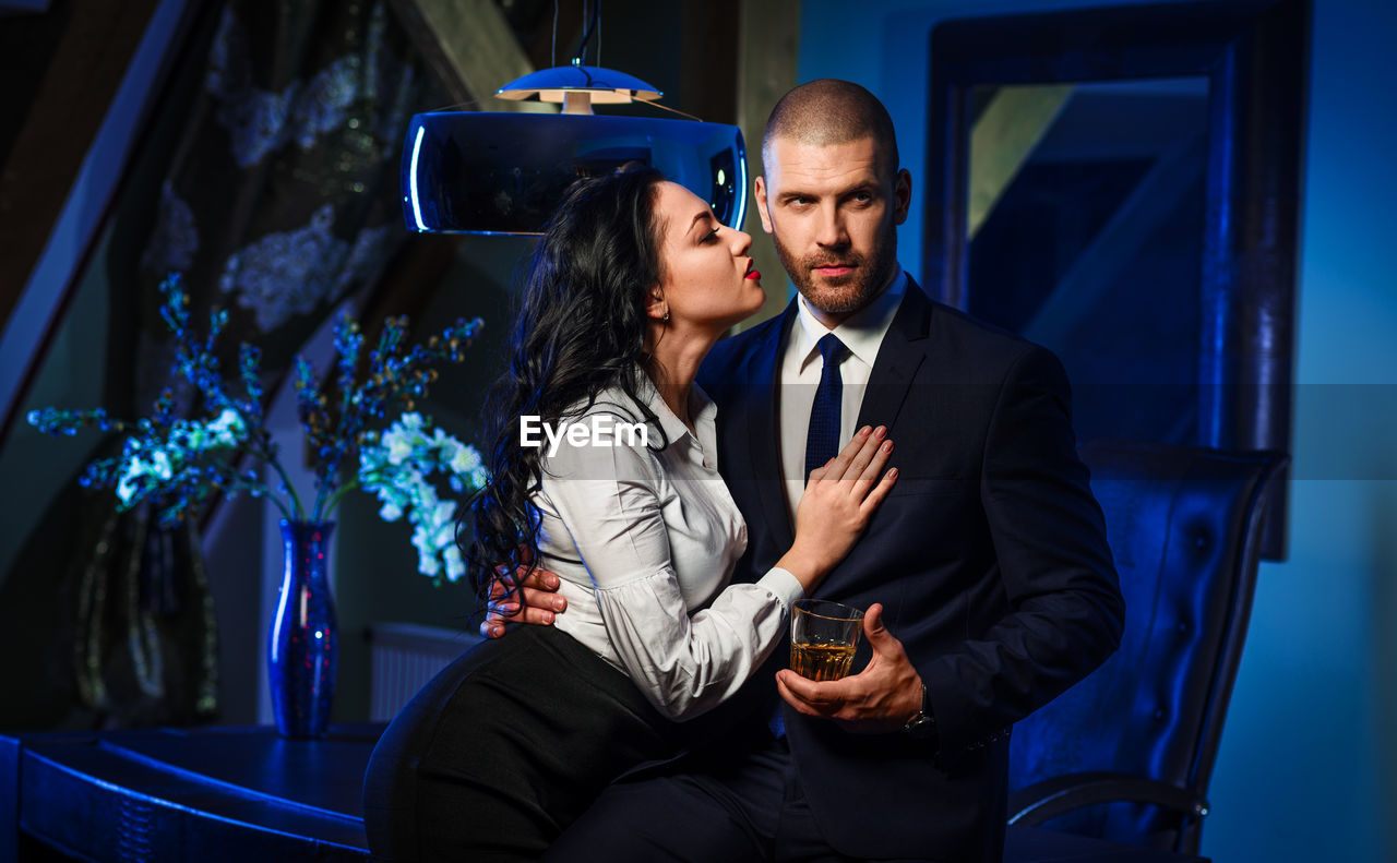 Businessman holding alcohol while standing with romantic woman in office