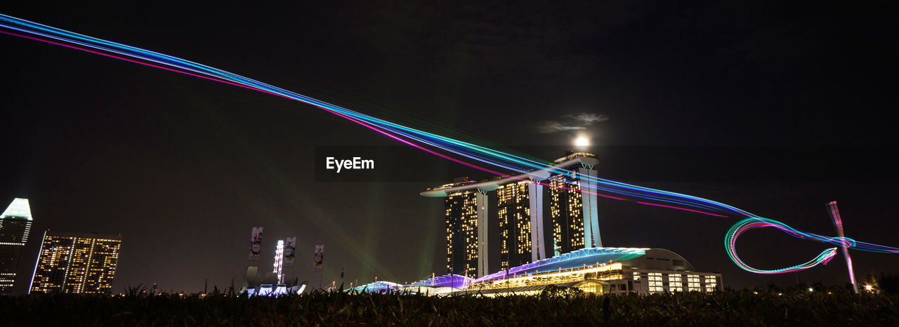 Panoramic view of light trails against illuminated marina sands bay