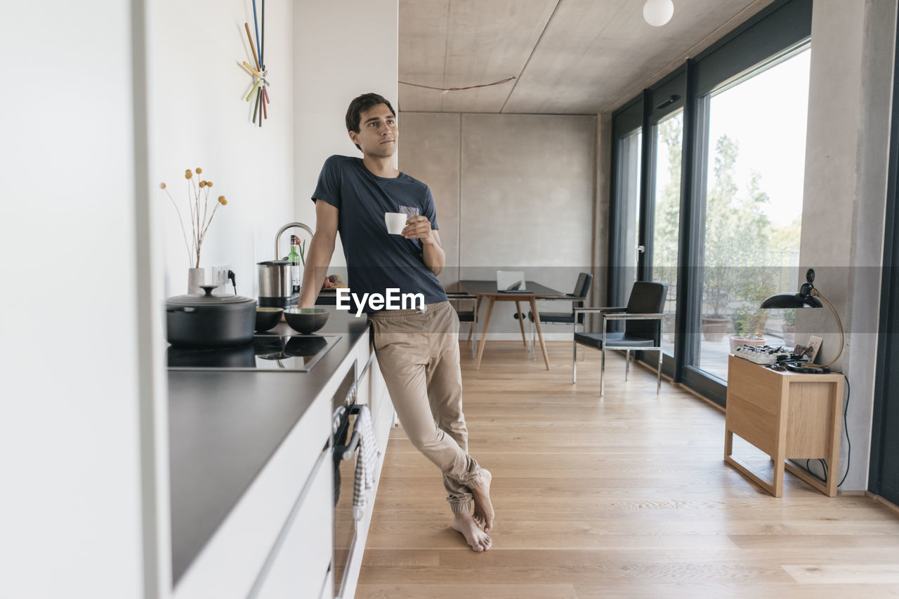 Young man holding cup of coffee in kitchen at home