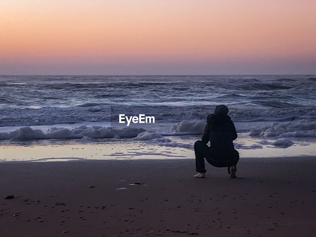 Rear view of woman on beach against sky during sunset