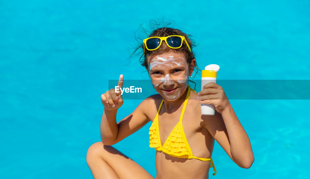 Portrait of girl applying suntan lotion by pool