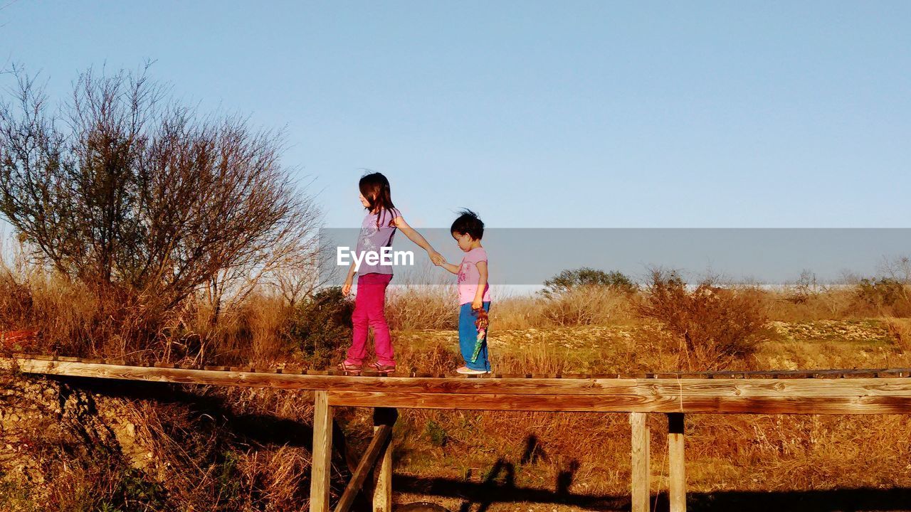 Side view of girls walking on wooden bridge
