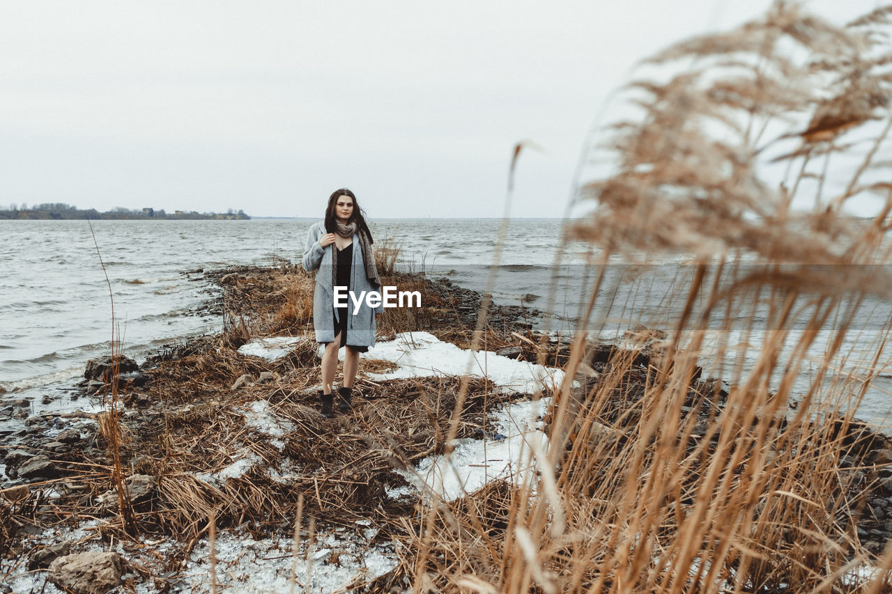 Young woman standing on shore against sky