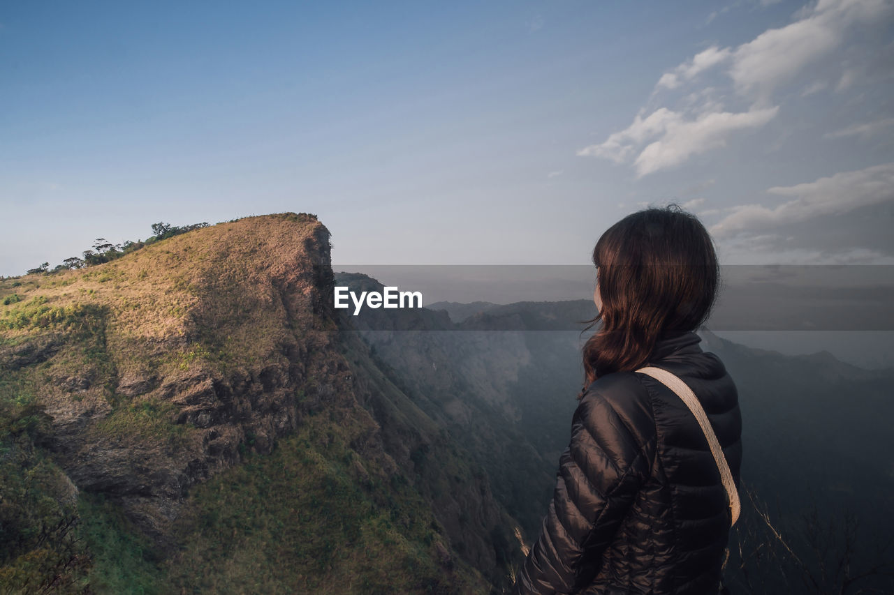 Woman looking at mountain while standing against sky