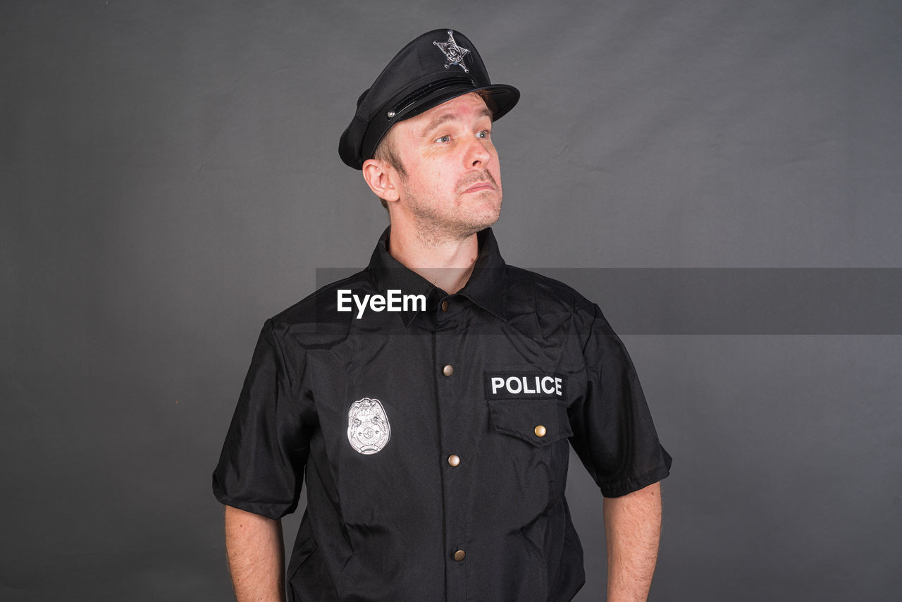 studio shot, uniform, adult, one person, clothing, portrait, authority, men, government, occupation, police force, standing, protection, security, law, police officer, person, indoors, black, mature adult, badge, cap, serious, hat, copy space, pocket, front view, looking at camera, cut out, waist up