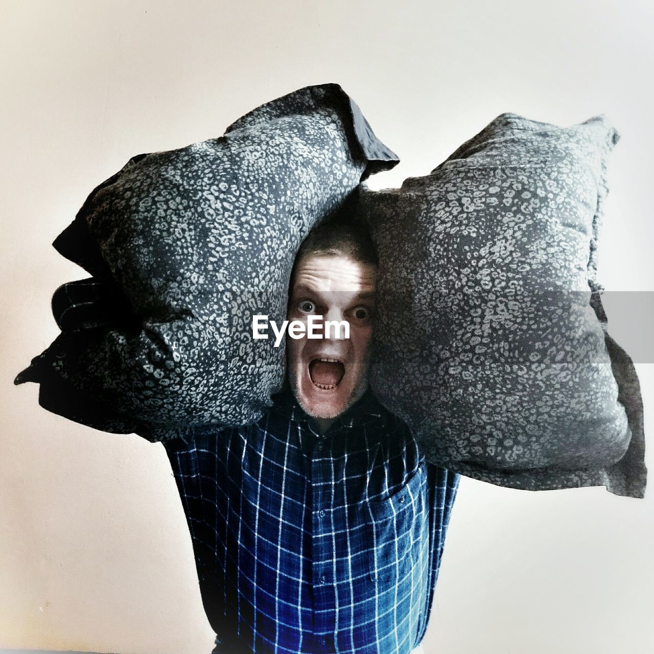 Portrait of man screaming while carrying pillows against white background