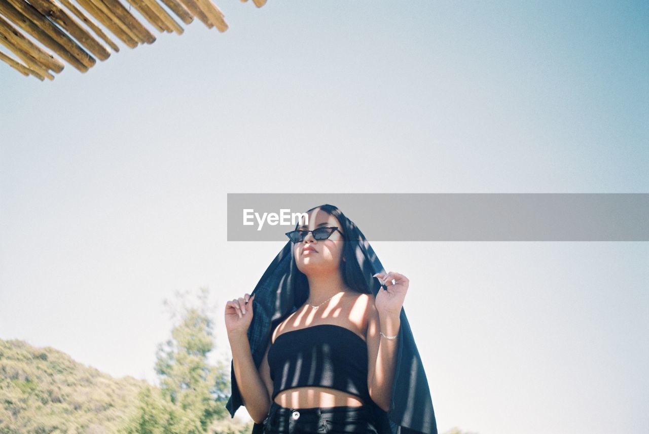 Low angle view of woman wearing sunglasses against clear sky