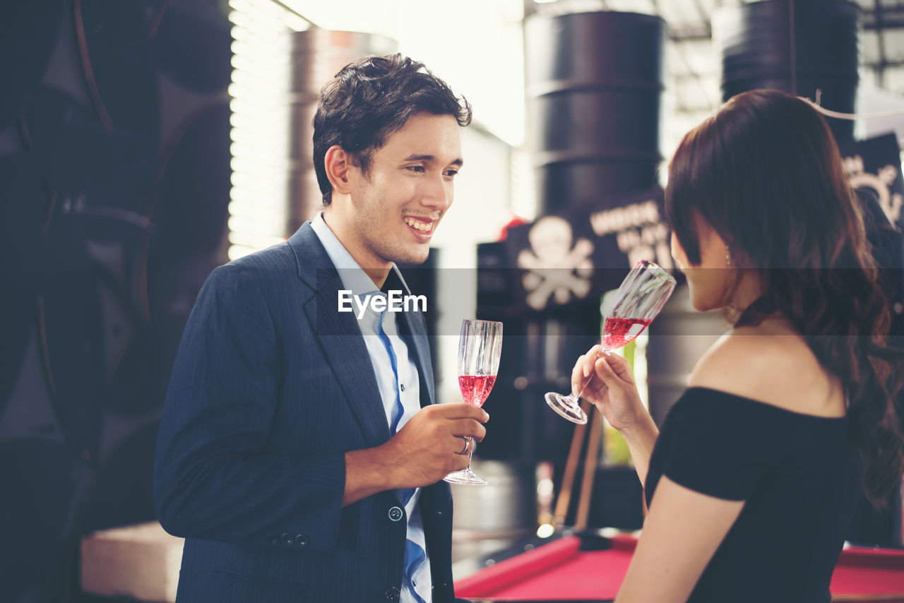 Smiling couple toasting red wineglasses while standing in bar