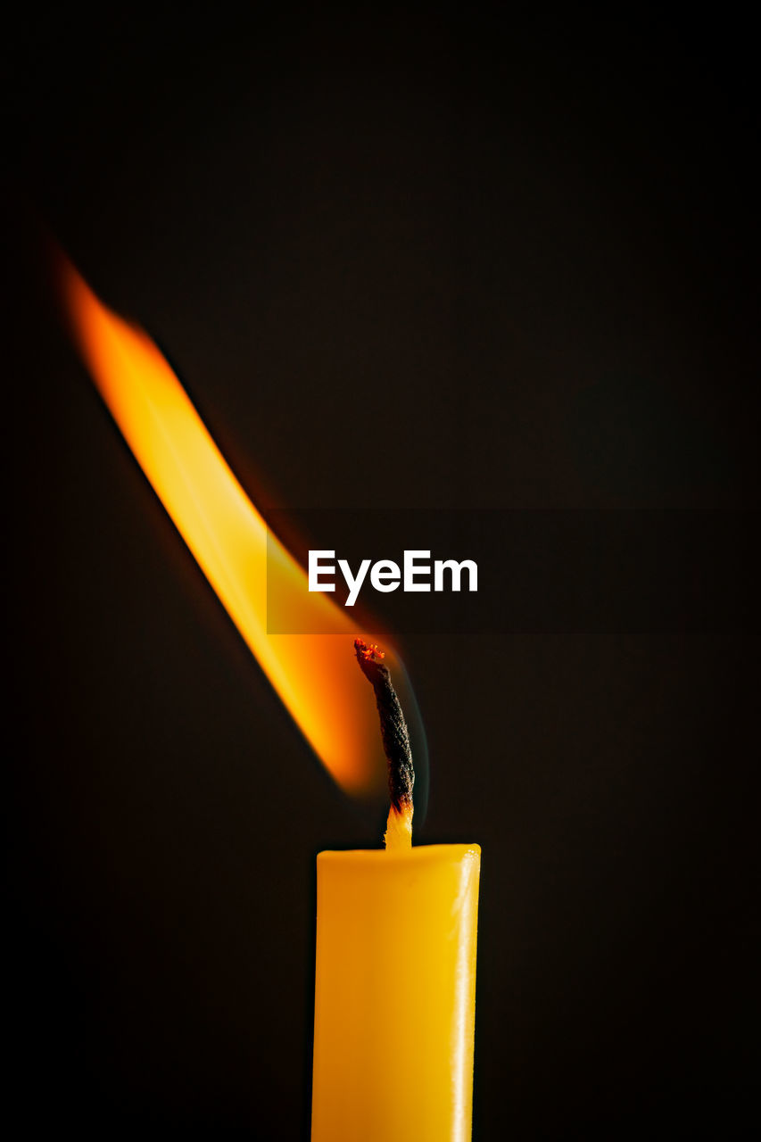 Close-up of a yellow candle illuminated in a black background.