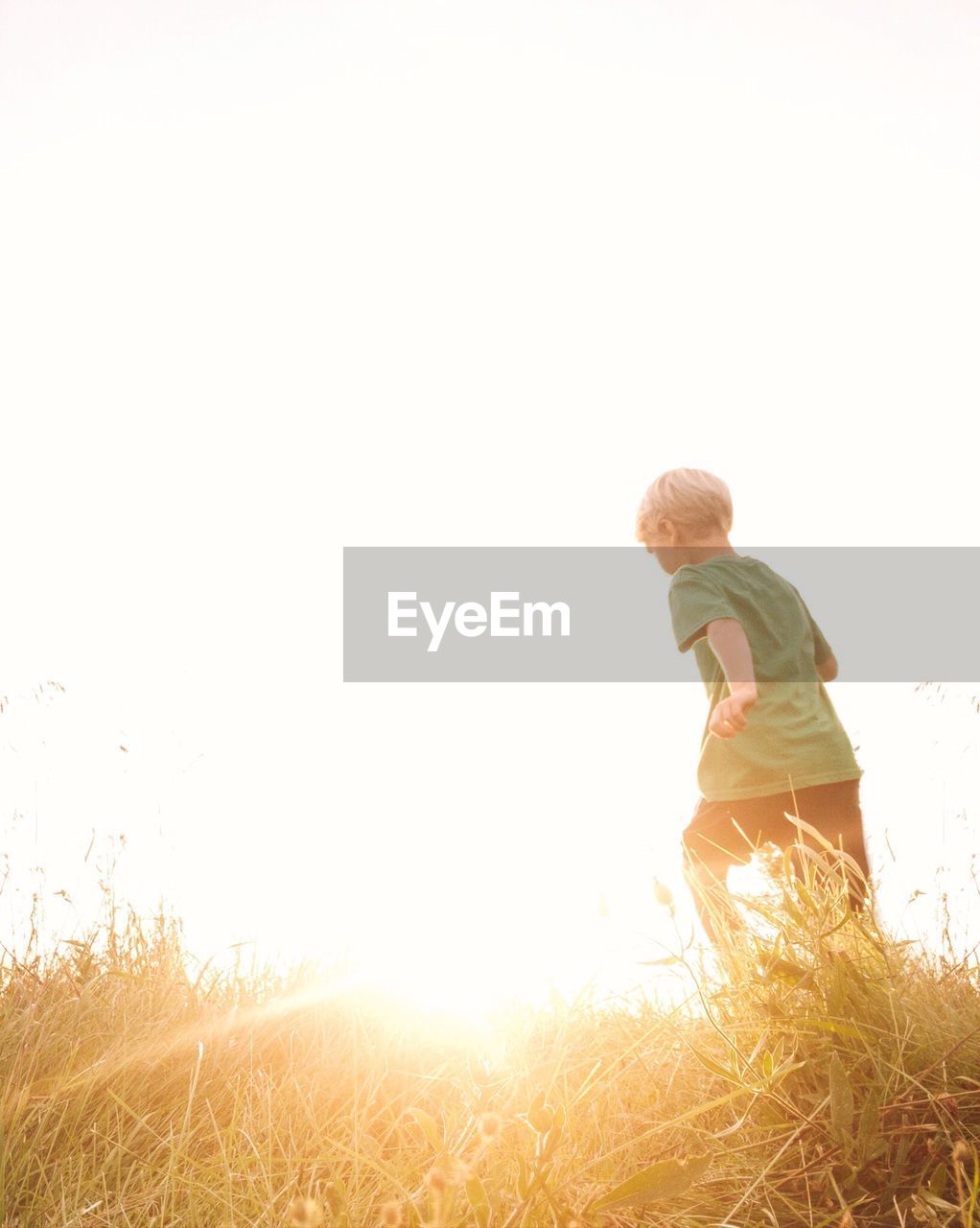 Rear view of boy running on field against clear sky