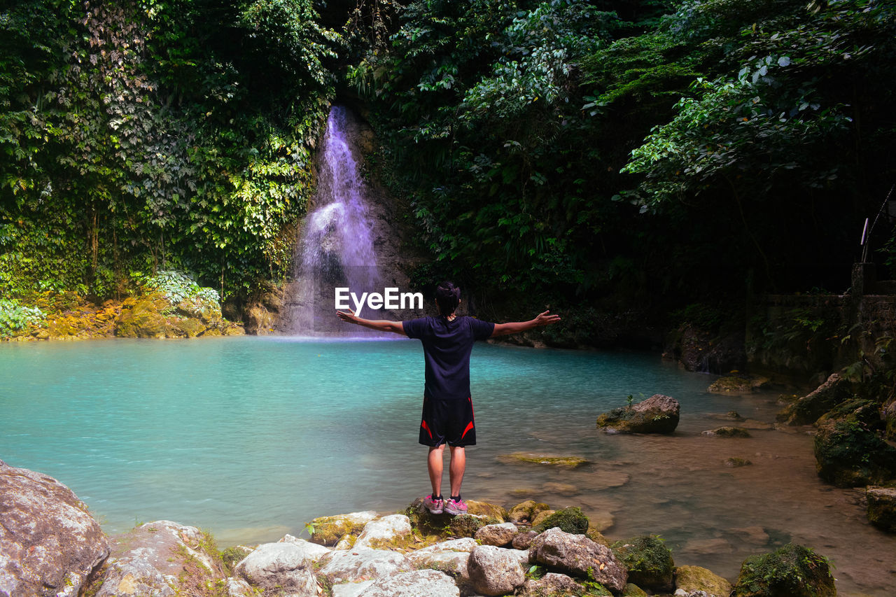 REAR VIEW OF WOMAN STANDING BY WATERFALL